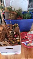 Mixed Christmas decorations in boxes including ornaments, a decorative planter, faux pine branches, berries, twig reindeer, and Christmas books.