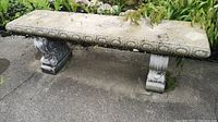 Front view of the concrete bench showing the rectangular seat and two pedestal legs with decorative scrollwork, exhibiting weathered surface and outdoor patina.