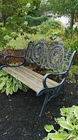 Full view of the garden bench showing cast iron frame with detailed Victorian style medallion backrest and weathered wooden seat slats.