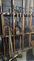 Full view of garden tools hanging on rack including shovels, rakes, and cultivators.