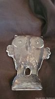 Clear glass owl figurine with distinct spiral eye details and textured base, sitting on brown fabric background.