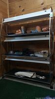 Full view of chrome metal frame shelving with three shelves fitted with fluorescent grow lights and black removable trays. Top shelf holds terra cotta pots and decorative terra cotta figurines. Middle shelf has plastic containers and raised planter trays. Bottom shelf contains a rolled mat and electrical cord.