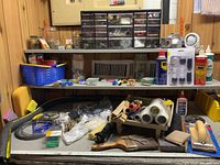 Wide photo of workbench with multiple hardware boxes, wire spools, paint supplies, and tools arranged on the shelf and desk