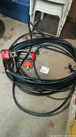 Coiled black garden hose with blue stripes and three sprinklers including Dramm and Gardena visible on cement floor.