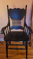 Full view of black painted wooden chair showing carved back, armrests, and turned legs
