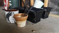 All items in lot showing two long black plastic balcony planters, medium and small terra cotta pots, and a ceramic paint splatter pot.