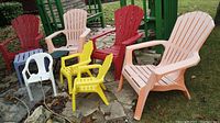 Wide view of all chairs including 4 adult Muskoka chairs in peach, beige, and red; 2 yellow child-size Muskoka chairs; 1 white child-size plastic chair; grouped on stone patio.