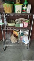 Full view of the chromed metal wire shelving unit with three shelves and various items displayed to show size and shelving style. Shelves are wire mesh and unit is on casters.