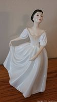 Front view of Royal Doulton Donna porcelain figurine holding skirt with painted facial details.