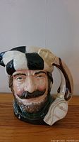 Front view of the Royal Doulton Toby Jug "Trapper" showing the detailed face with a black and white checkered hat and rifle handle.