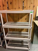 Plastic 4-shelf storage unit with slatted shelves against a wooden panel wall, beige with gray trim.