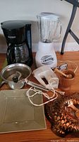Full view of the lot showing coffee maker, blender, hand mixer, mortar and pestle, copper fish mould, ricer, and ceramic plate on floor.