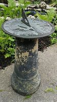 Photo showing sundial face with engraved Roman numerals and motto, mounted on weathered cylindrical concrete pedestal.