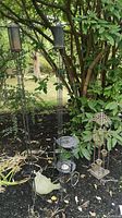 Two tall black metal garden torches, a cast iron plant stand, a tall metal candle holder with multiple glass votives, and a concrete bird on the ground.