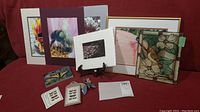 All items grouped together on couch including framed photo, matted photos, painted plastic panel, decorative butterfly, and book.