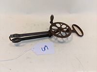 Side view of antique primitive cast iron Dover egg beater, showing gear wheel, wooden handle knob, and cast iron blades