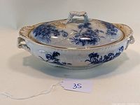 Front angled view of Flow Blue covered oval vegetable dish showing detailed blue floral pattern, shaped handles, and lid with handle.