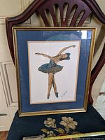 Full frontal photo of the framed ballerina gouache painting resting on a chair, showing the ballerina in blue tutu and the signature on the artwork.