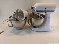 Front and contents showing white KitchenAid mixer with two stainless steel bowls and attachments inside one bowl.