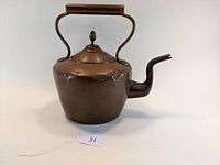 Front and left side view of the large copper tea kettle showing the fixed handle, domed lid with finial, curved spout, and smooth copper body with small dents.