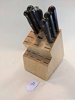 Front view of the wooden knife block holding seven knives with black handles and metal rivets, plus a sharpening steel.
