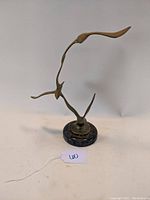 Front view of brass bird sculpture mounted on round dark marble base showing three abstract birds in flight.