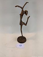 Brass dancing girl statue, front view with one leg raised and arms extended upward and outward.