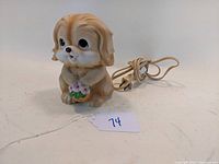 Porcelain puppy dog lamp holding basket of pink flowers with power cord, shown from front left angle.