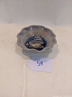 Front view of ceramic dish showing scalloped edges and embossed sailboat design with blue background.
