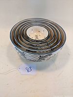 Side view of all six nested mixing bowls showing hand-painted floral and geometric designs on white ceramic.