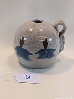 Front side view of the round pottery vase showing the single curled handle and blue flower decorations.