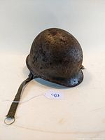 Front and side views of a rusted steel Vietnam era military helmet showing the overall condition and attached canvas chin strap.