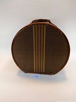 Front view of 1940s vintage round train hat case, showing brown fabric with vertical stripes and leather trim.