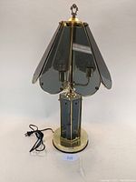 Front view of vintage lamp showing smoke-colored glass shade panels and brass base with attached power cord.