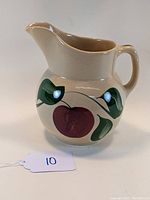 Front view of the ceramic pitcher showing the apple pattern and handle on cream background.