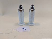 Pair of white milk glass Westmoreland salt and pepper shakers with silver tops, showing front view and intricate paneled grape pattern embossed on glass.