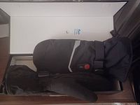 Photo of a pair of large black heated mittens with adjustable straps and heat control buttons inside a box.