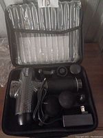 Photo showing Leopal massage gun, four different shaped massage heads, charger with USB cable inside black zippered carrying case with mesh pocket.