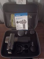 Matte black Renpho mini massage gun and four attachments organized in a black zippered hard carrying case, along with user manual.