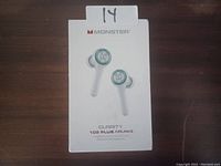 Photo of original retail box showing Monster Clarity 102 Plus Airlinks wireless in-ear headphones in white with green accents. Box placed on dark wood surface with lot number 14 indicated.