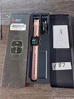 Orit pink smart watch inside original black box, showing watch face with digital display, pink silicone band, USB charging cable, and instruction manual.