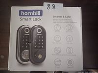 Two Hornbill smart locks shown on product packaging. The box highlights features such as key-free entry, app control, anti-theft alarm, auto-lock, micro USB backup, Bluetooth keypad, IC card, and fingerprint access.
