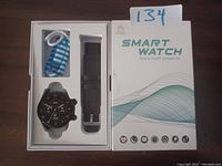Smart watch in original packaging with charging cable and extra watch band visible