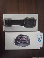Black digital smart watch inside white box with an image of the watch on the front.