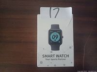 Photo of white retail box for smart watch labeled "Your Sports Partner" showing watch face with time, date and fitness icons.