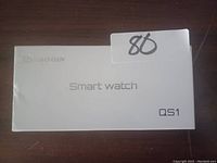Photo of white rectangular box for Smart Watch QS1 showing brand and model details