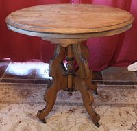 Front and side view of oval stripped wood top table with ornate turned central column and carved castered legs.