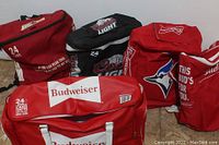 Overview of five beer chiller bags including insulated backpacks and duffle bags with Budweiser, Coors Light, Canadian, and Blue Jays branding