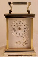 Front view of Bulova quartz carriage clock showing white dial with Roman numerals and engraved floral design below face.