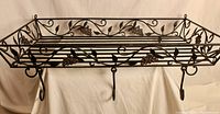 Front view of the wrought iron hanging pot rack showing its rectangular frame, grapevine decorations, and hooks beneath.